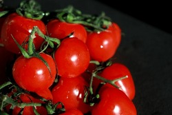 close up of bunch of fresh cherry tomatoes with green stems isolated on dark grey background