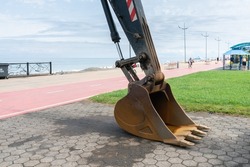Excavator bucket on the background of the cloudy sky and sea on a summer day