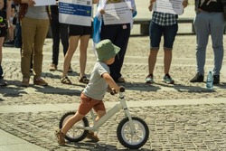 A little boy on a balance bike against the background of adult activists of the anti-war protest of free Russians against military aggression on a sunny day on a cobbled old square in Krakow, Poland