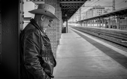 Portrait of adult man on cowboy hat waiting in train station. 