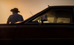 Portrait of adult man in cowboy hat standing against a vintage car during sunset