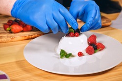 Chef hands with gloves cooked. Chef  is cooking dessert with berries.
