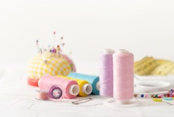 Sewing supplies on a white wooden table: sewing thread, scissors, a large spool of thread, pieces of cloth, needles,centimeter, buttons