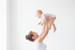 Happy young mother lifting cute baby up high in air, spending and enjoying time together with daughter