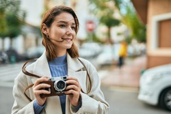 Young hispanic tourist woman smiling happy using vintage camera at the city