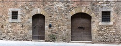 Doors and windows in old medieval stone walls along a street in a tuscan village.