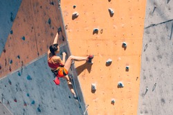 Training at the city climbing gym. A strong woman climbs a climbing route on artificial terrain. Slim girl involved in sports.