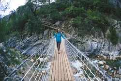 A woman travels alone in picturesque places. A girl with a backpack crosses the canyon on a suspension bridge. A woman walks along a mountain trail alone. Walk through the woods.