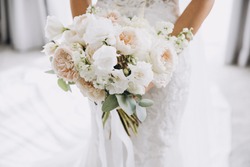 young girl in a white wedding dress holds in her hands a bouquet of flowers and greenery with a ribbon