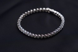 Platinum bracelet with diamonds on black silk background. White gold bracelet with gemstones, close-up. Elegant woman jewelry