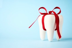 Dental treatment concept. Dental offers free treatment. White tooth model with red bow ribbon on a blue background with copy space, close-up