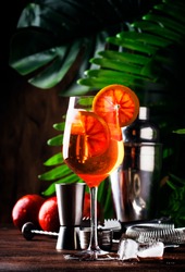 Aperol spritz cocktail in big wine glass with bloody oranges, summer Italian fresh alcohol cold drink. Wooden bar counter background with tools, summer mood concept with palm trees, selective focus