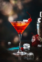 Manhattan alcoholic cocktail with bourbon, red vemuth, bitter, ice and cocktail cherry in glass, night mood image, copy space