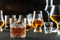 Hard strong alcoholic drinks and distillates in glasses in assortment: vodka, cognac, tequila, scotch, brandy and whiskey, grappa, liqueur, vermouth, tincture, rum. Brown background