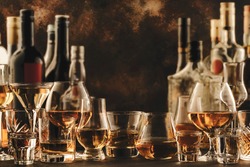 Hard strong alcoholic drinks and distillates in glasses and bottles in assortment: vodka, cognac, tequila, scotch, brandy and whiskey, grappa, liqueur, vermouth, tincture, rum. Brown background