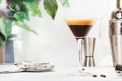 Espresso martini, trendy alcoholic cocktail with vodka, coffee liqueur, syrup and ice, black background, bar tools