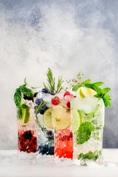 Cocktails or mocktails cold drinks. Classic summer refreshing long drink in highballs with berries, lime, herbs and ice on gray bar counter background