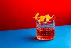 Sazerac cocktail with cognac, bourbon, absinthe, bitters, sugar and lemon peel. Dazzling red blue background with hard light and harsh shadows