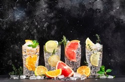 Gin tonic and citrus cocktails set. Alcoholic drinks with lime, lemon, grapefruit, orange, soda and herbs in highball glasses, black bar counter background. Summer cocktail party