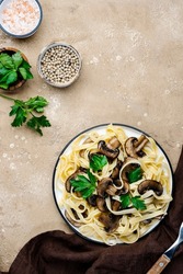 Cooked pasta with mushrooms with parsley on plate on beige stone kitchen table background, top view. Vegan cooking and eating, italian cuisine recipe