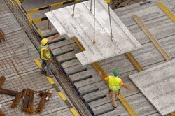 Workers on a construction site gettiing the concrete slab directed by a big crane