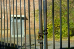 The old gates of the factory are locked with a rusty old chain around them. An old metal gate with a conventional lock holding several chains on it. Locked gate. No entry, restricted area