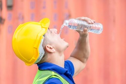 Worker man in hard hat drinking water at containers cargo