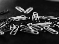 A grayscale selective focus shot of a scattered pile of paperclips with distant light on them