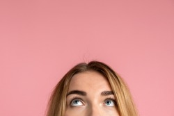 On a pink background, the half-face of a girl and her eyes looking up. Place for advertising, copy space.