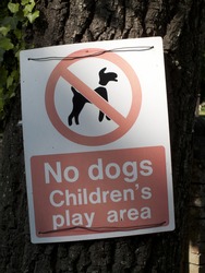 No dogs childrens play area warning sign mounted on tree trunk