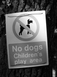 Monochrome no dogs childrens play area warning sign mounted on tree trunk