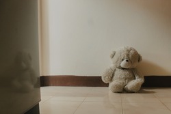 Teddy bear sitting alone at the wall.