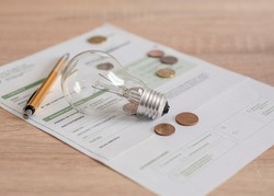 Electricity bill with light bulb, several coins and pen on the desk. Concept of electricity prices and tax payments.