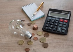light bulb with coins, notebook with a pen and calculator on a wooden background