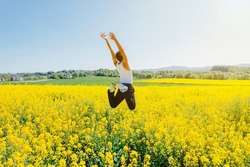 Rear view of a a young homosexual boy jumps in a yellow rapeseed field. Concept of a good mood and summer vacation. Copy space.