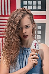 Blonde curly girl holding a big ice cream with a serious look in a blue tunic with blue manicure