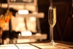 Shot of the champagne glass on a wooden table. Sunlight and bubbles.