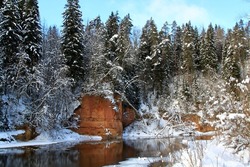 Winter view on a river coast with a red rock and forest covered with white snow. Selective focus. High quality photo