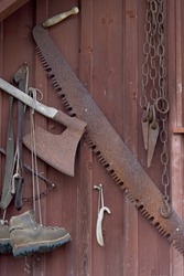 Close up of old wooden facade decorated with suspended rusted historical tools like axe saw chain wedges and mountain boots as a concept for old craftsmanship
