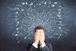 Businessman covering face on chalkboard background with drawn arrows. Risk and confusion concept 