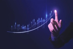 Close up of hand pointing at glowing business chart on dark blue background. Stock, market and trade concept. Double exposure