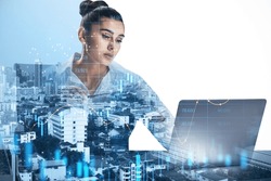 Attractive young european businesswoman using laptop on abstract blue city background with index, candlestick forex chart and mock up place. Success, fintech, transform and trade concept.