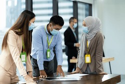 Group of diverse corporate colleagues wearing protective medical face mask for health, brainstorming, sharing ideas on table office. Muslim woman in medical face mask working her colleagues in office