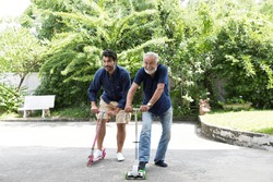 Senior father with adult son playing scooter together in the backyard at home. Elderly man people and young man playing scooter at the playground with happy and fun