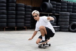 Asian young man skater riding on skateboard on courtyard with wear sunglasses. Young man teenager skateboarding outdoor