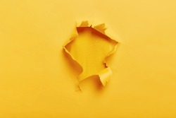 Small paper hole with torn sides over yellow background for your text, print or promotional content. Through paper. Ripped hole. No people. Accurate shot. Advertising and breakthrough concept