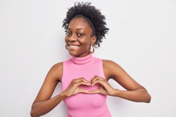 Beautiful dark skinned woman gesture heart over chest expresses love says be my valnetine smiles positively stands romantic against white wall admires something gives positive feedback. I like you