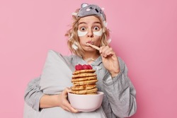 Amazed young pretty woman brushes teeth going to eat pancakes for breakfast and undergoes beauty procedures shocked to wake up very late and being in hurry poses indoor. Morning routine concept