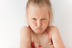 Small girl with blond pony-tail looking seriously, folding hands and frowning eyebrows. Her gloomy appearance says she is very unhappy and offended. Blond baby showing disapproval with pursed lips.