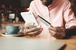 African American man in casual shirt paying with credit card online while making orders via the Internet. Successful black businessman making transaction using mobile bank application. Selective focus